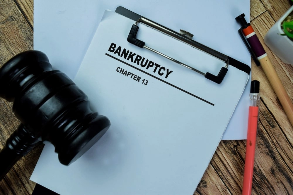 A clipboard with a document labeled "Bankruptcy Chapter 13" next to a judge's gavel, pen, and pencil on a wooden desk.